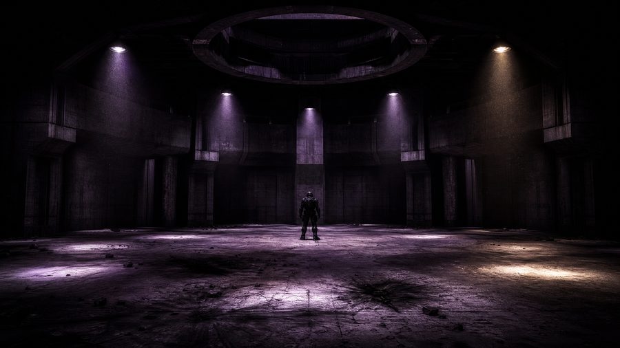 A lone armoured figure standing in an empty concrete arena under overhead lamps